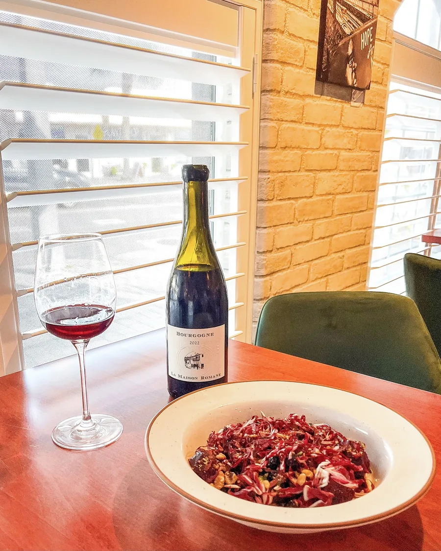 A bottle of Bourgogne and a poured glass beside a radicchio salad by the window