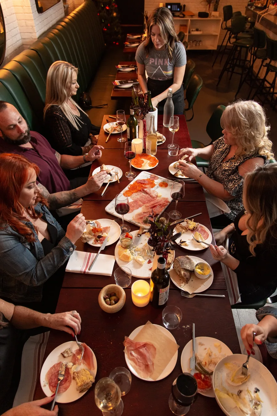 A long table of guests sharing charcuterie and wine while a server pours