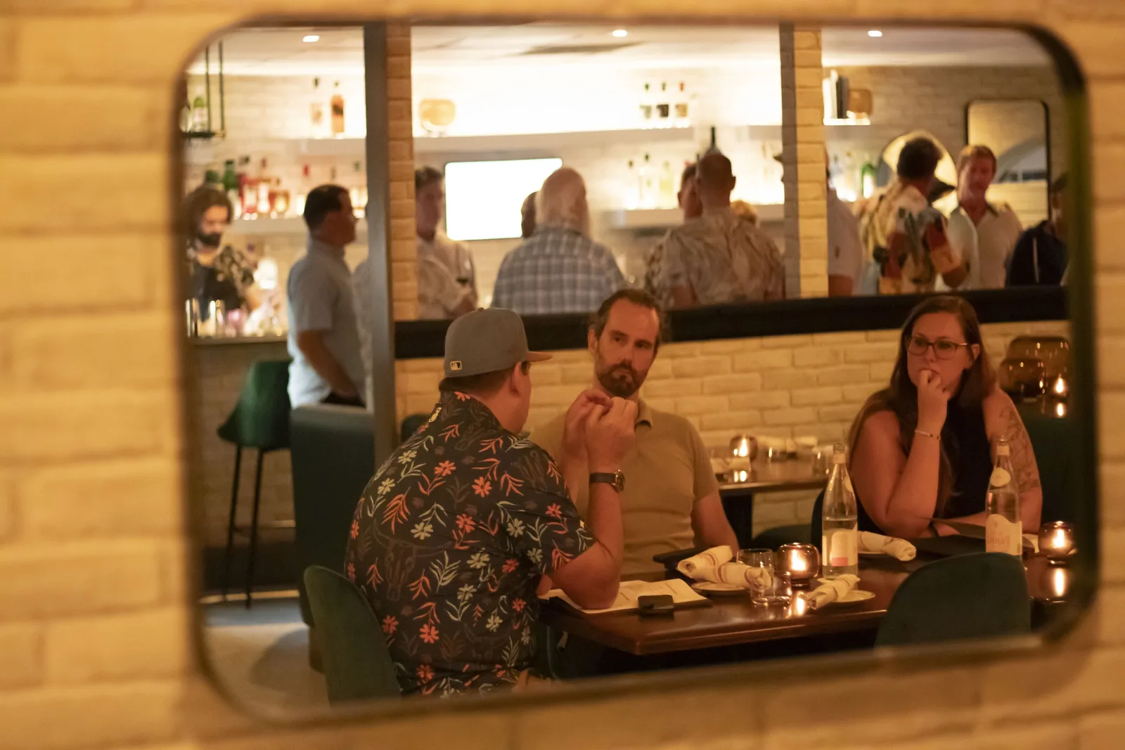 Guests at dinner, caught in the reflection of a wall mirror
