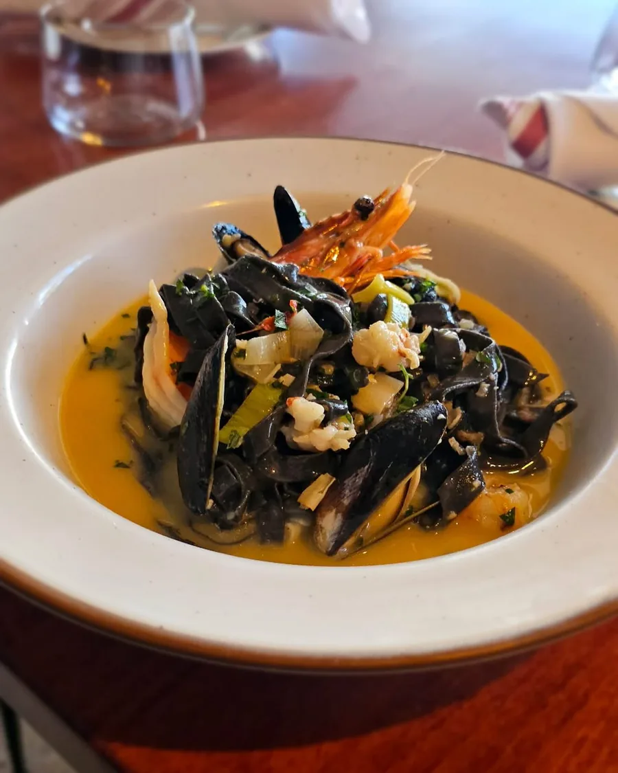 Squid ink pasta with mussels and a whole prawn in a shallow bowl
