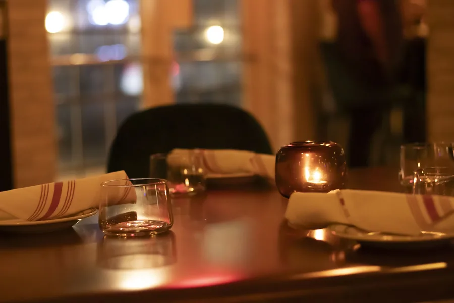 A candle burning on a laid table, glasses waiting